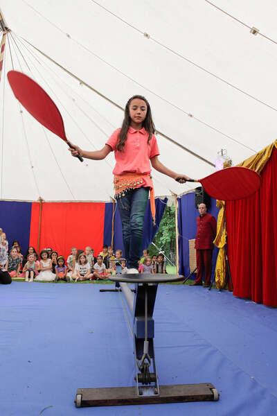 Mädchen balanciert auf einem Seil und hält zwei rote Fächer zum ausbalancieren in der Hand