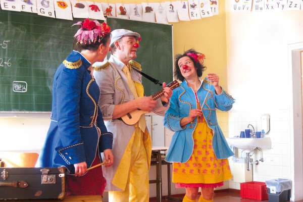 Drei Clowns der ROTE NASEN beim Musizieren in einem Klassenzimmer.