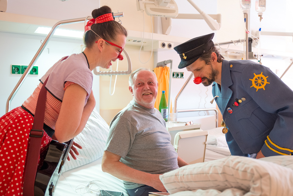 Zwei Clowns interagieren mit Mann im Spitalsbett