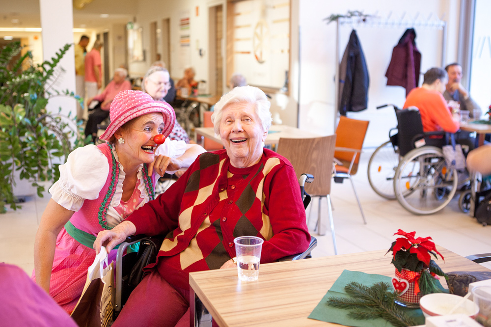 Clownin im Dirndl und Seniorin lachen in die Kamera