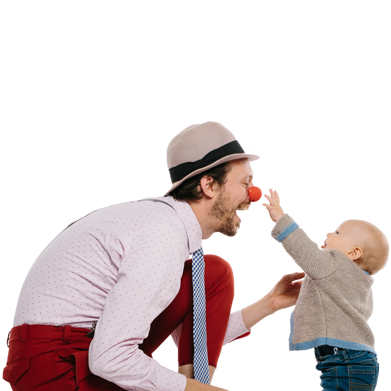 Baby greift Clown begeistert an die Clownnase und lächelt