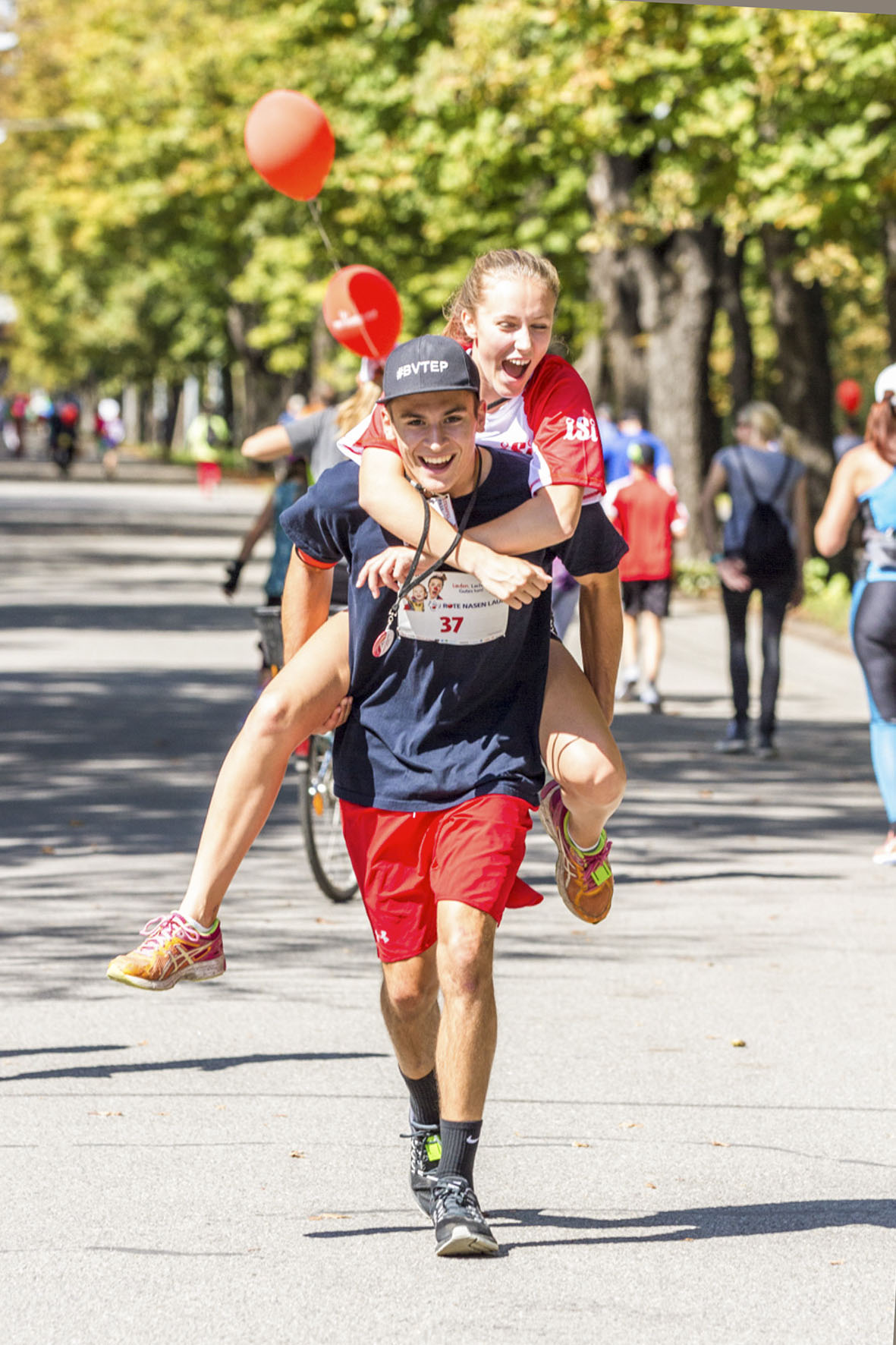 EinLäufer trägt eine Läuferin am Rücken und läuft lachend mit ihr durch das Ziel 
