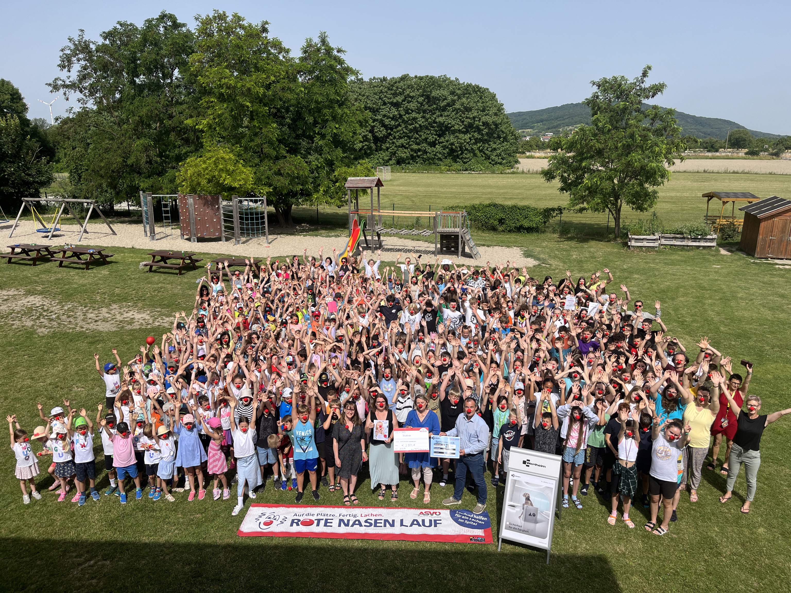 Eine große Gruppe von Kindern und Erwachsenen, die fröhlich die Arme nach oben strecken.