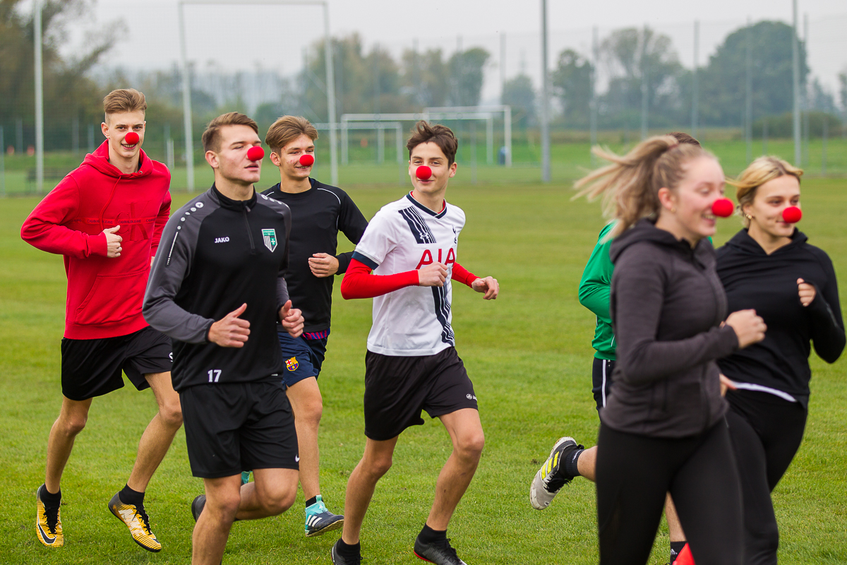 Schüler*innen des BORG Güssing laufen mit aufgesetzter roter Schaumstoffnase am Sportplatz.