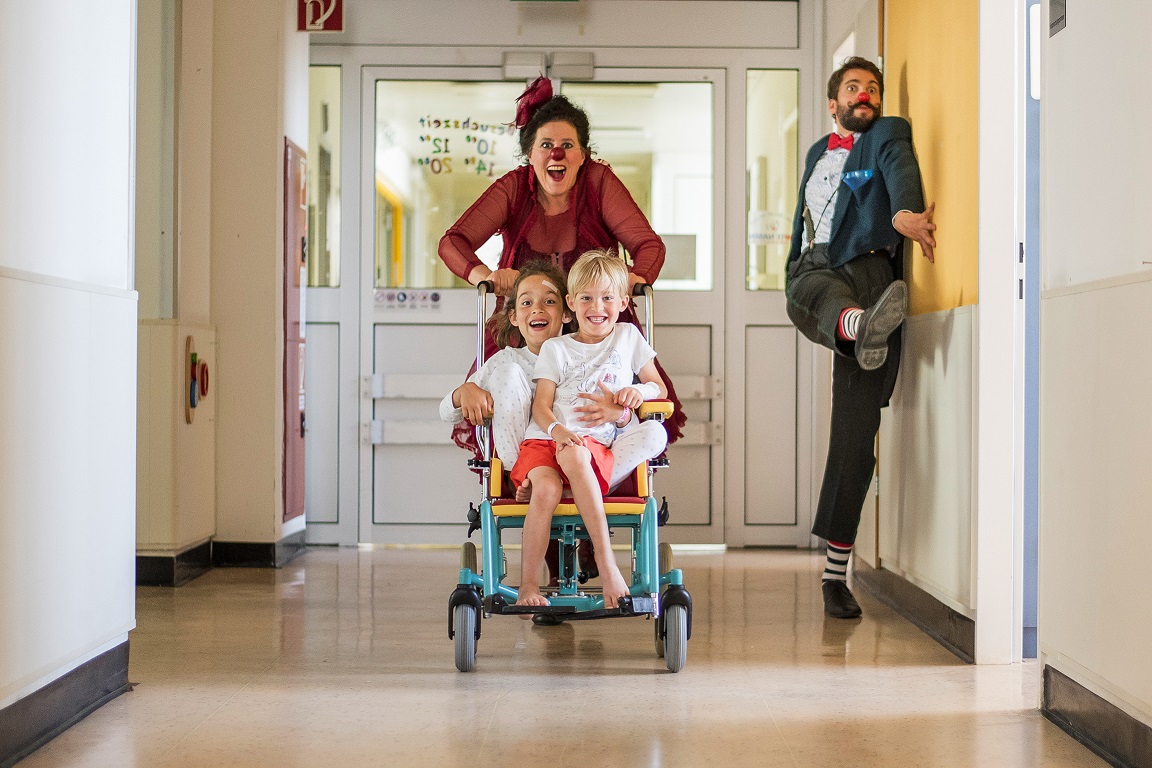 ROTE NASEN-Clown Robert und eine Clown-Kollegin führen zwei Kinder im Rollstuhl spazieren.