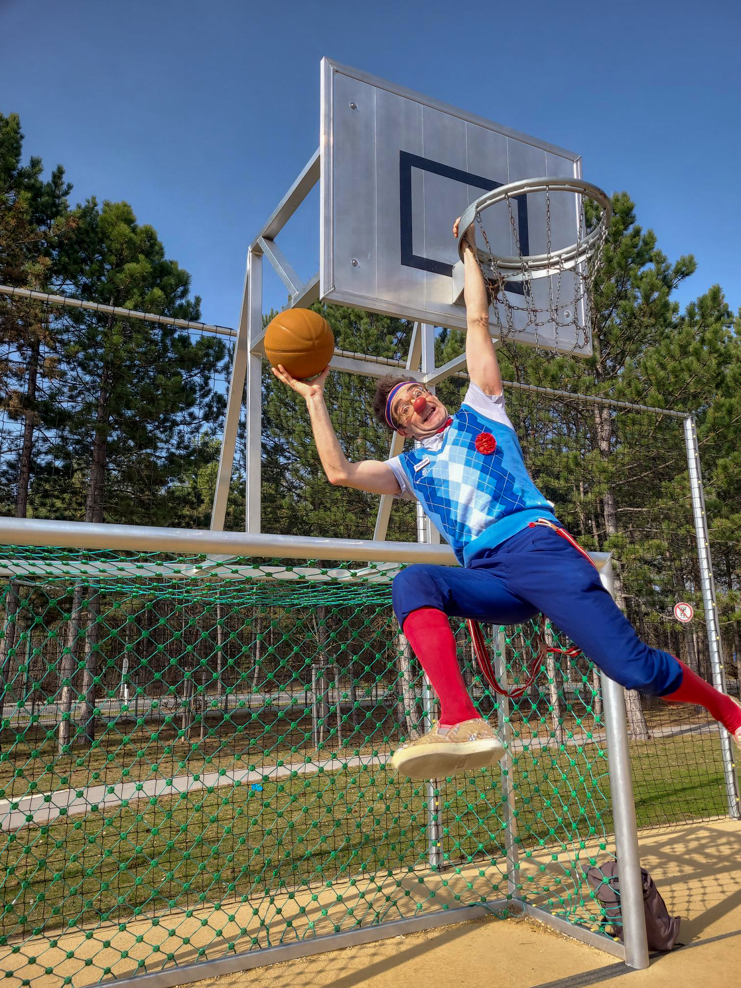 Clown Bernhart hängt auf einem Basketballkorb und wirft einen Ball.