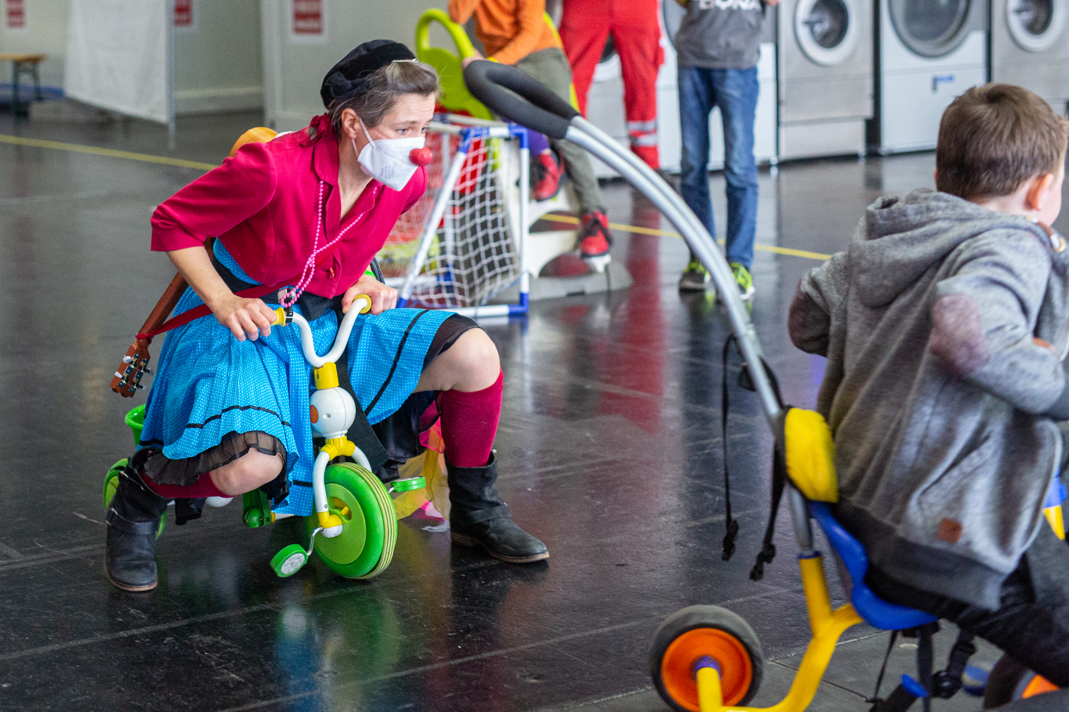 ROTE NASEN-Clownin Irmi und ein kleiner Junge fahren mit einem Kinderdreirad.