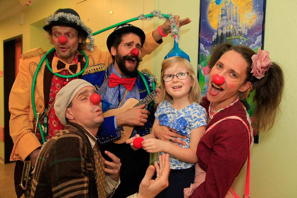 Gruppe von vier Clowns halten ein kleines blondes Mädchen hoch, alle Clowns singen