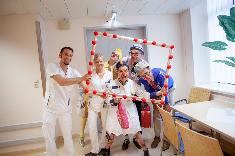 Pflegepersonal und Clowns posieren mit einem überdimensionalen Bilderrahmen mit roten Schaumstoffnasen