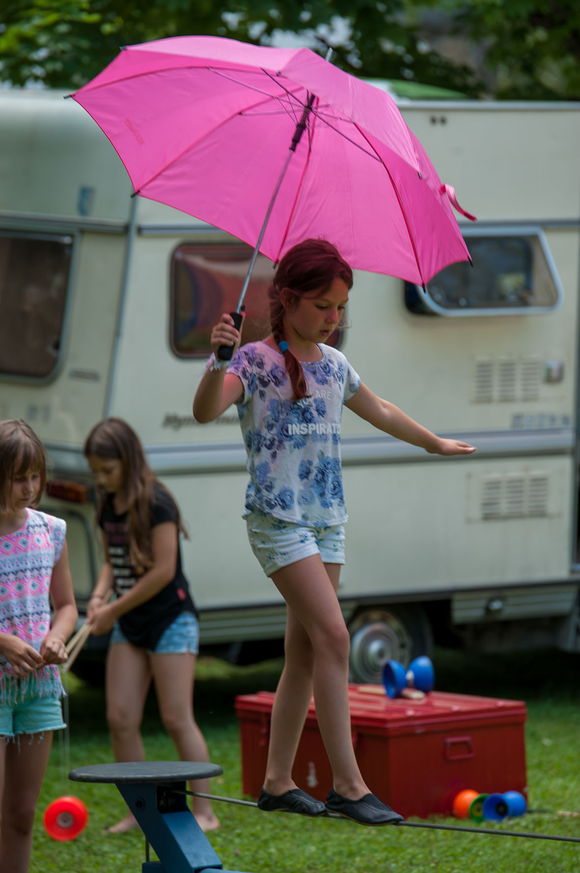 Mädchen mit pinkem Regenschirm balanciert auf einer Slackline
