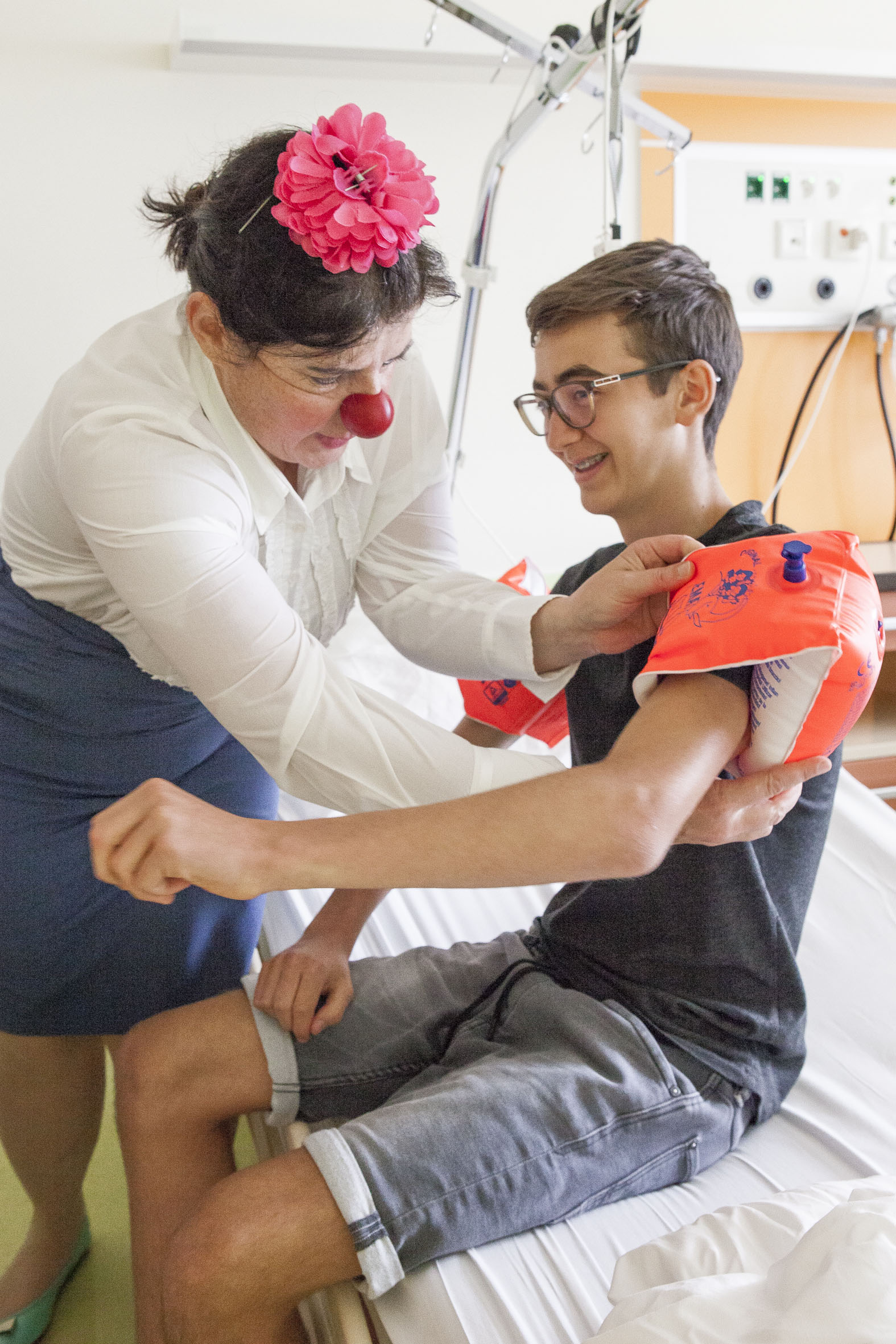 Clownin gibt Jungen im Krankenbett Schwimmflügeln auf den Arm