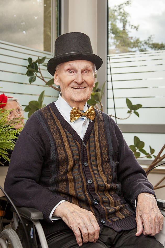 Senior sitzt lächelnd im Rollstuhl und trägt Zylinder und Fliege