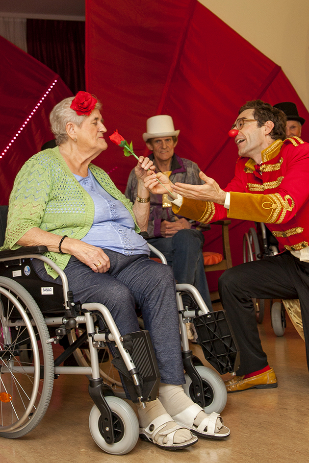 Seniorin im Rollstuhl bekommt von einem Clown eine Rose