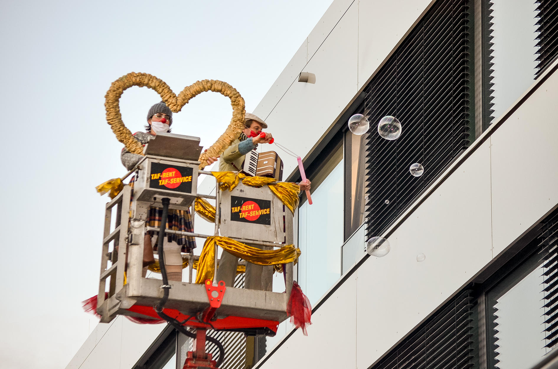 Clowns der ROTE NASEN auf einer Arbeitsbühne beim Erzeugen von Seifenblasen.