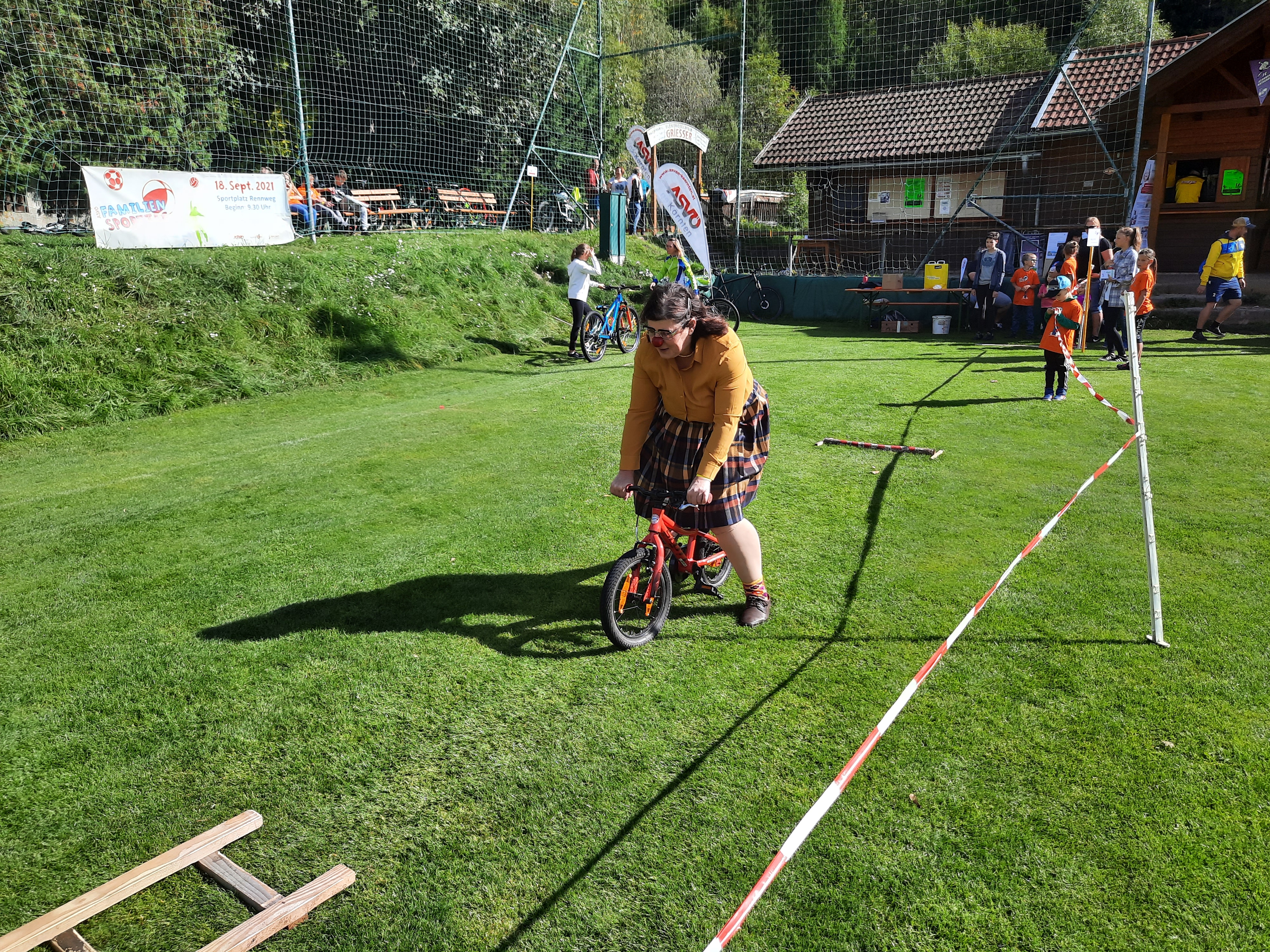 ROTE NASEN-Clownin Aloisia fährt mit einem Kinderfahrrad auf einer Wiese.