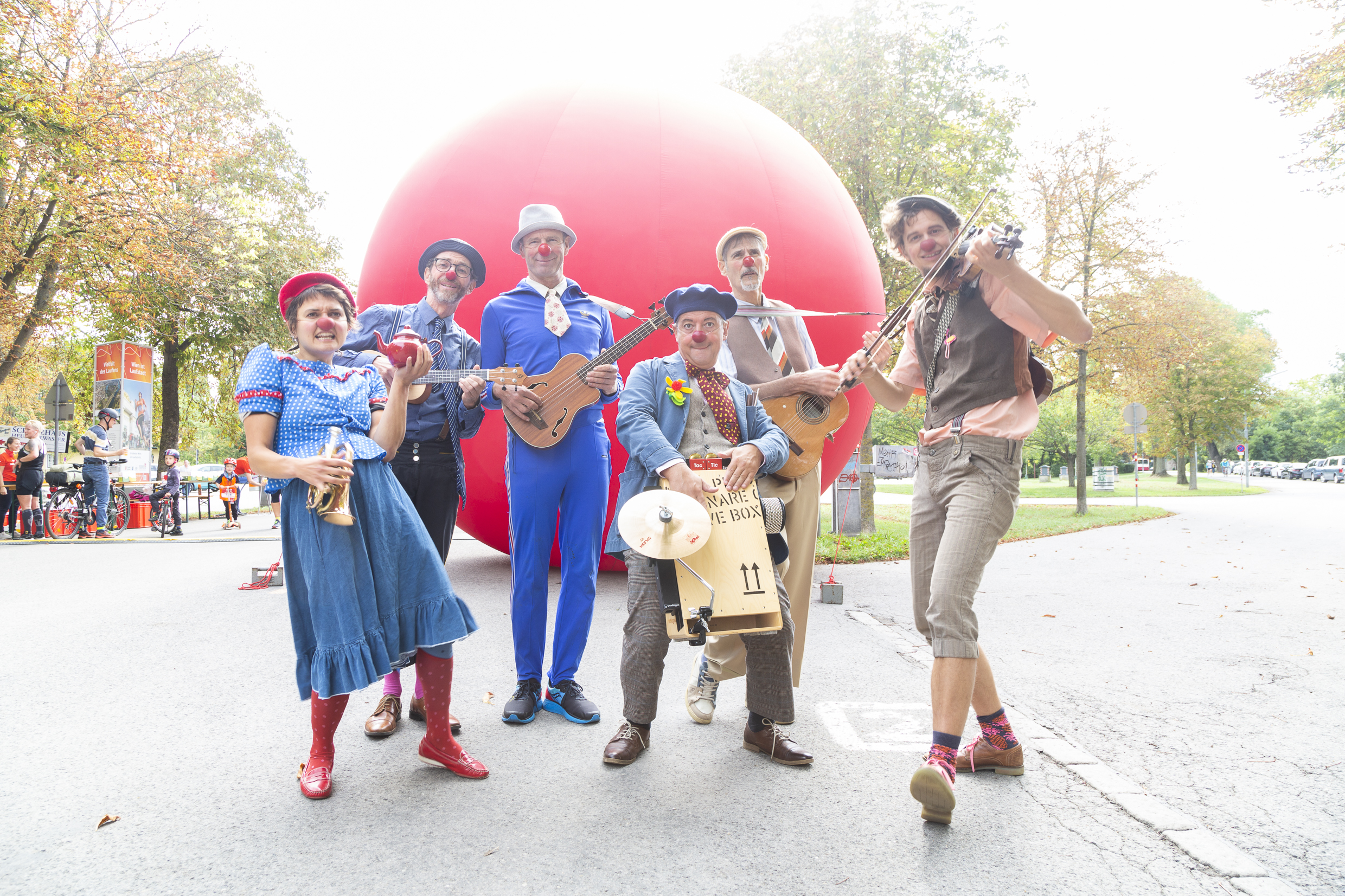 ROTE NASEN-Clowns musizieren vor einer großen, roten, aufblasbaren Nase.