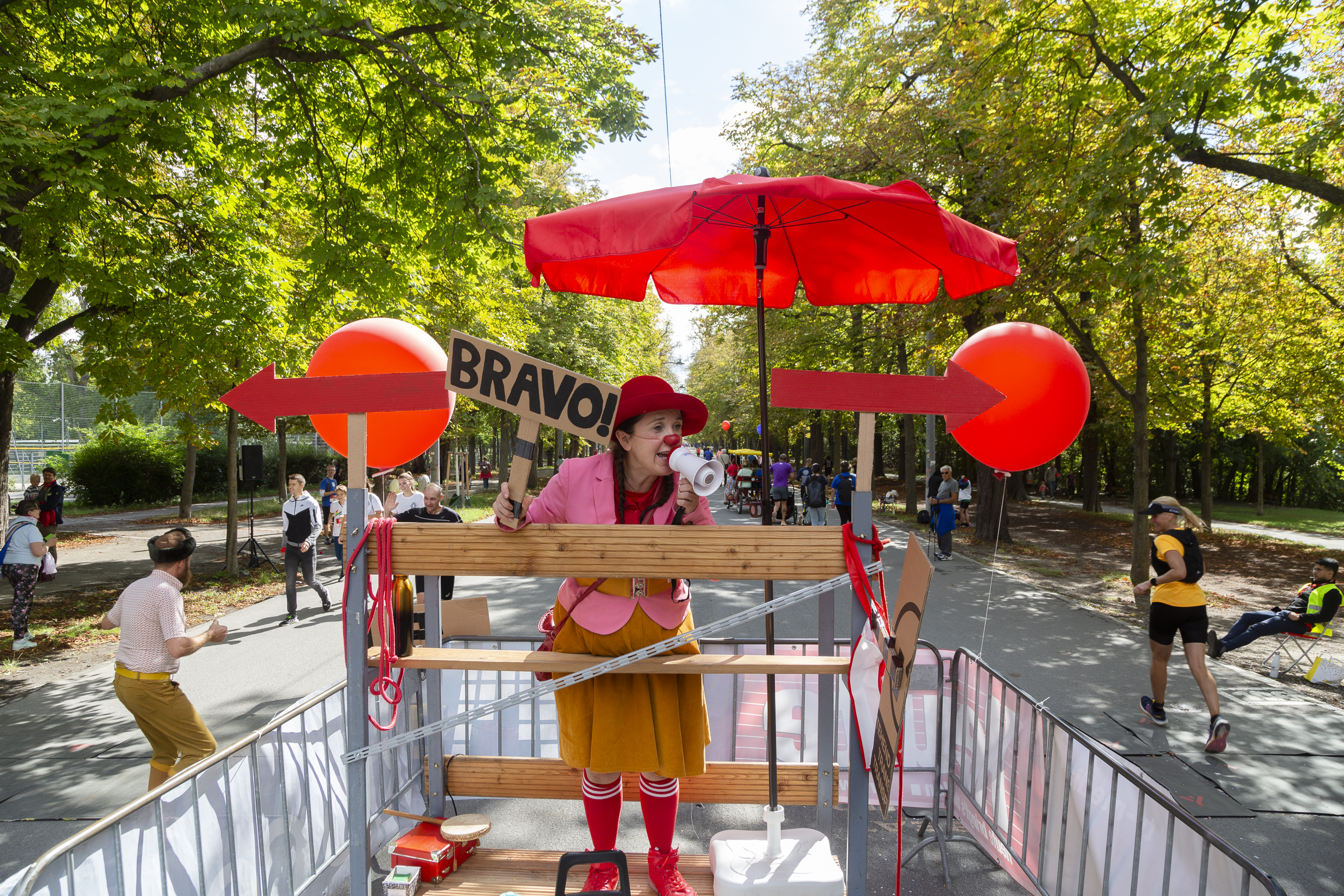 ROTE NASEN-Clownin Dagmar hält ein Schild mit der Aufschrift "BRAVO!" in der rechten und in der linken Hand ein kleines Megafon.