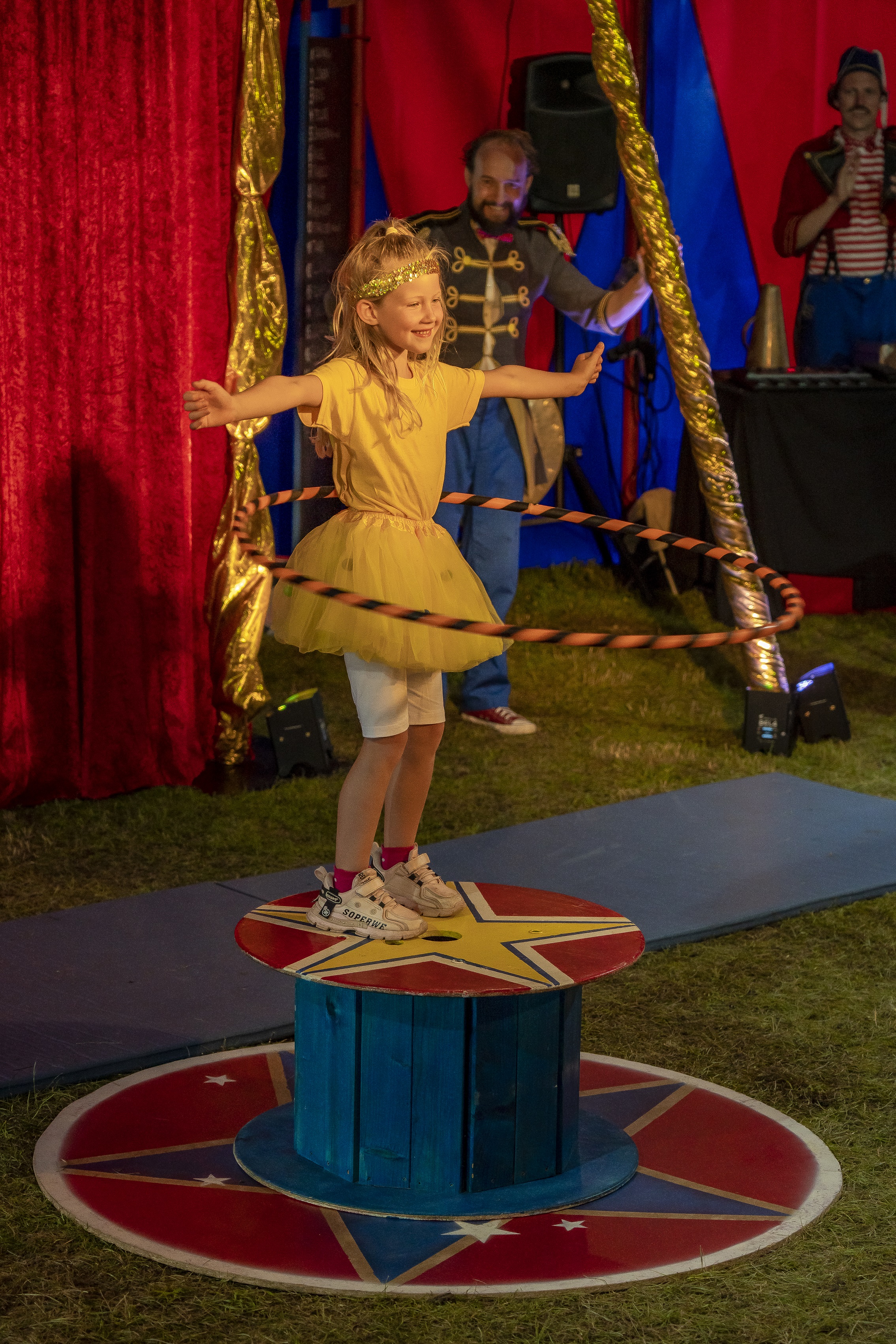 Ein kleines Mädchen steht auf einem Podest und schwingt einen Hula-hoop-Reifen.