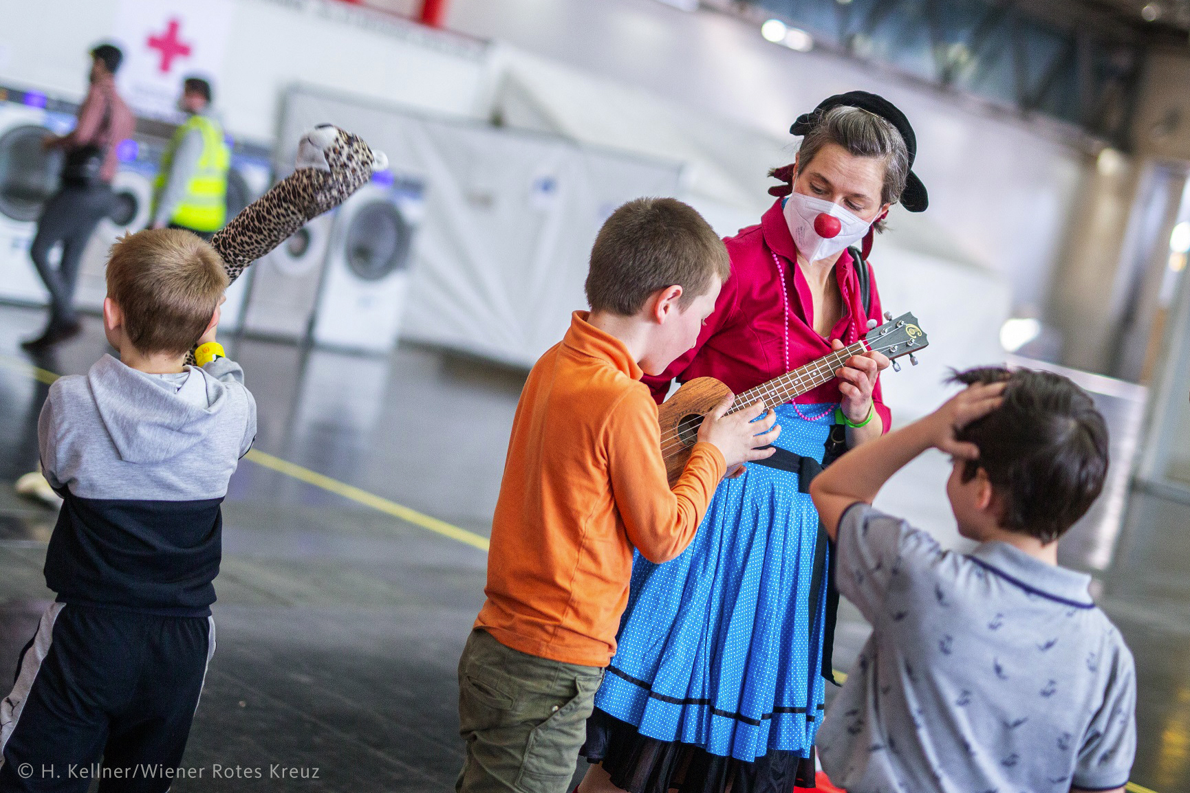 ROTE NASEN-Clownin Irmi mit Ukulele vor Kindern anlässlich des Weltflüchtlingstags 2022 in der Messe Wien.