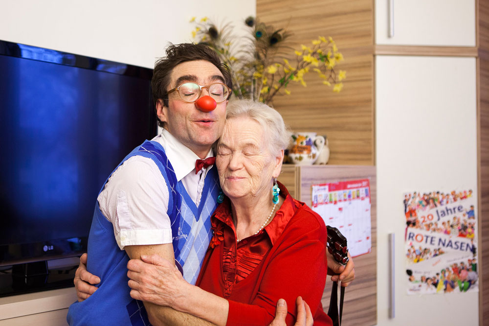 Clown Bernhart wird von Seniorin umarmt die dabei die Augen entspannt geschlossen hat