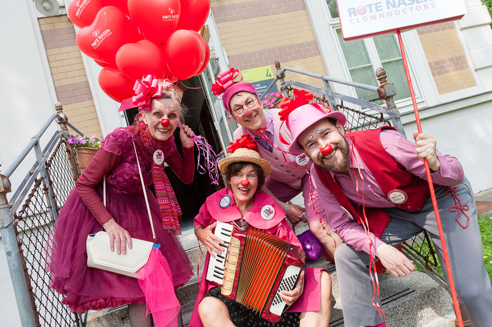 Gruppe von Clowns in rosa Outfits posiert für ein gemeinsames Foto, Herzförmige Luftballons sind auch am Foto