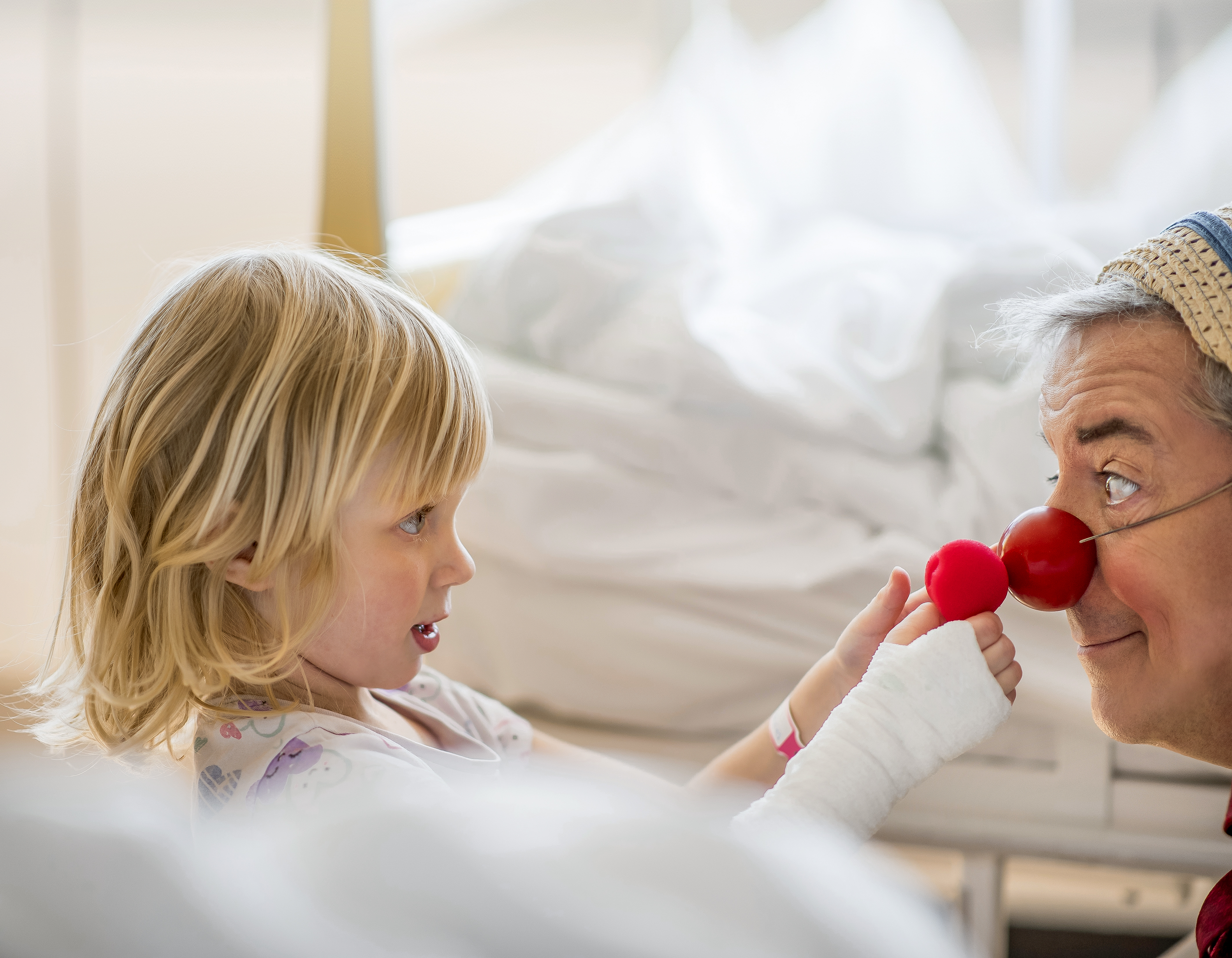 Clown unterhält Kind mit roter Schaumstoffnase im Spital.